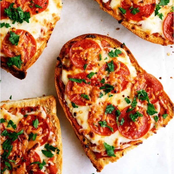 Four slices of pepperoni French bread pizza topped with melted cheese and chopped parsley on a white surface.