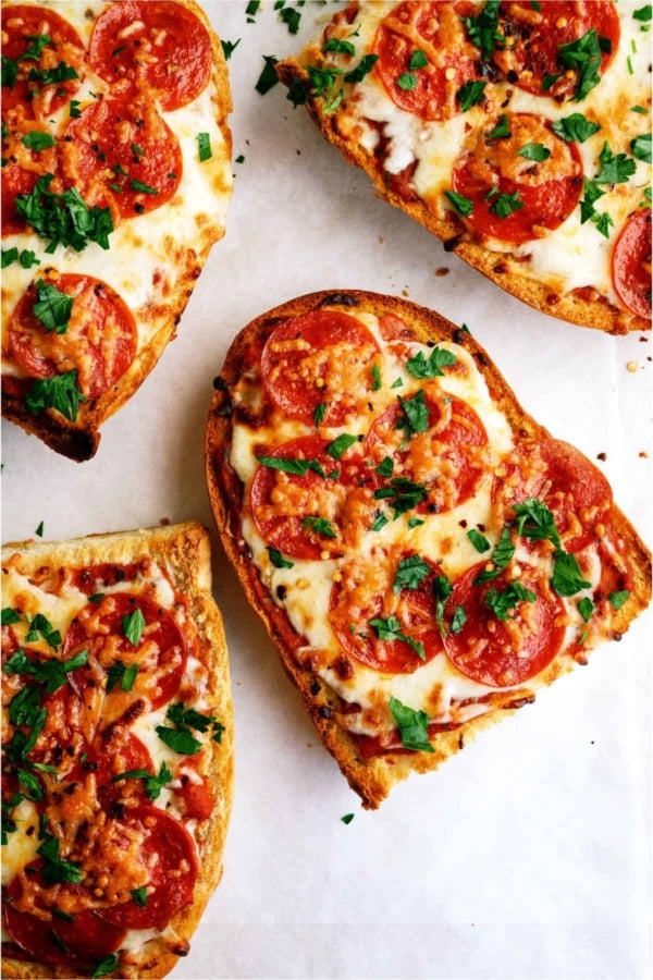 Four slices of pepperoni French bread pizza topped with melted cheese and chopped parsley on a white surface.