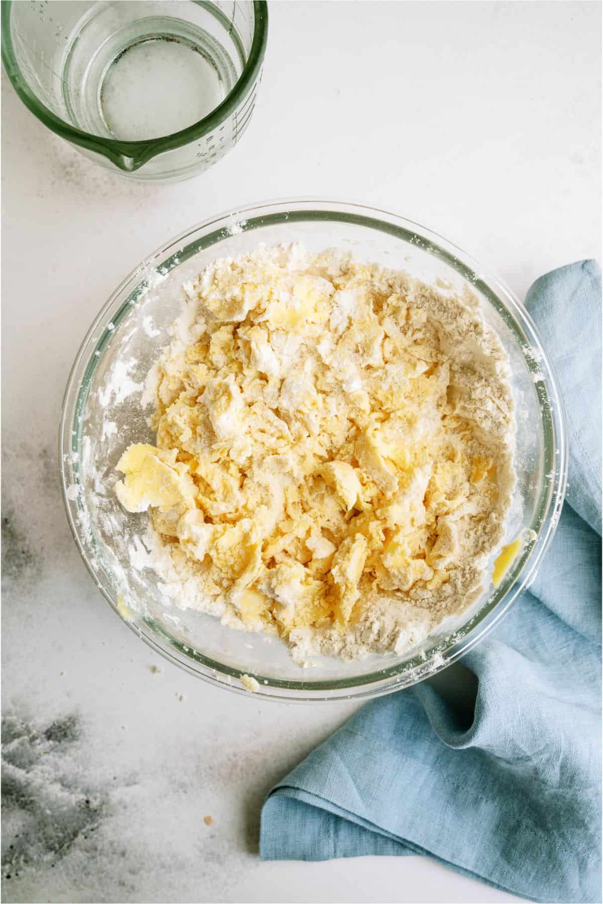 A mixing bowl with ingredients for homemade pie crust roughly mixed together.