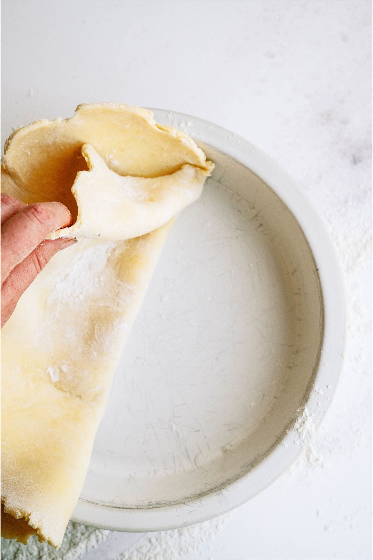 A hand laying a homemade pie crust in a pie pan.