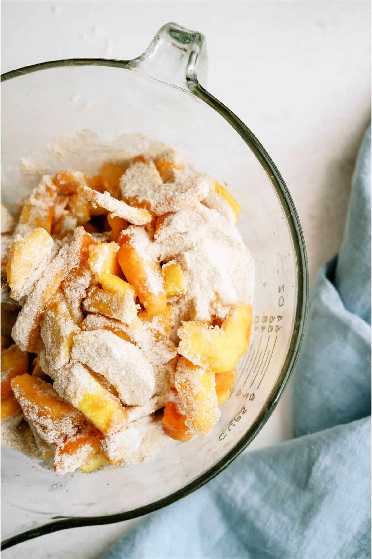 A glass mixing bowl with fresh peaches and dry ingredients.