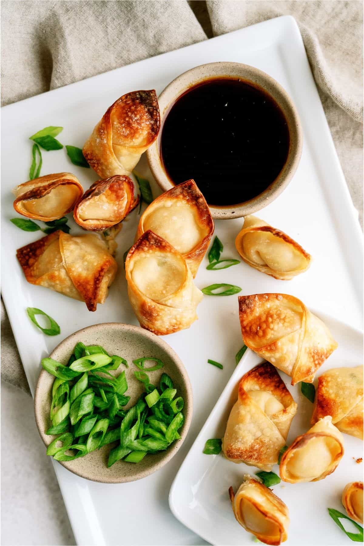 Crispy dumplings on a white plate with a small bowl of soy sauce and a side of sliced green onions.