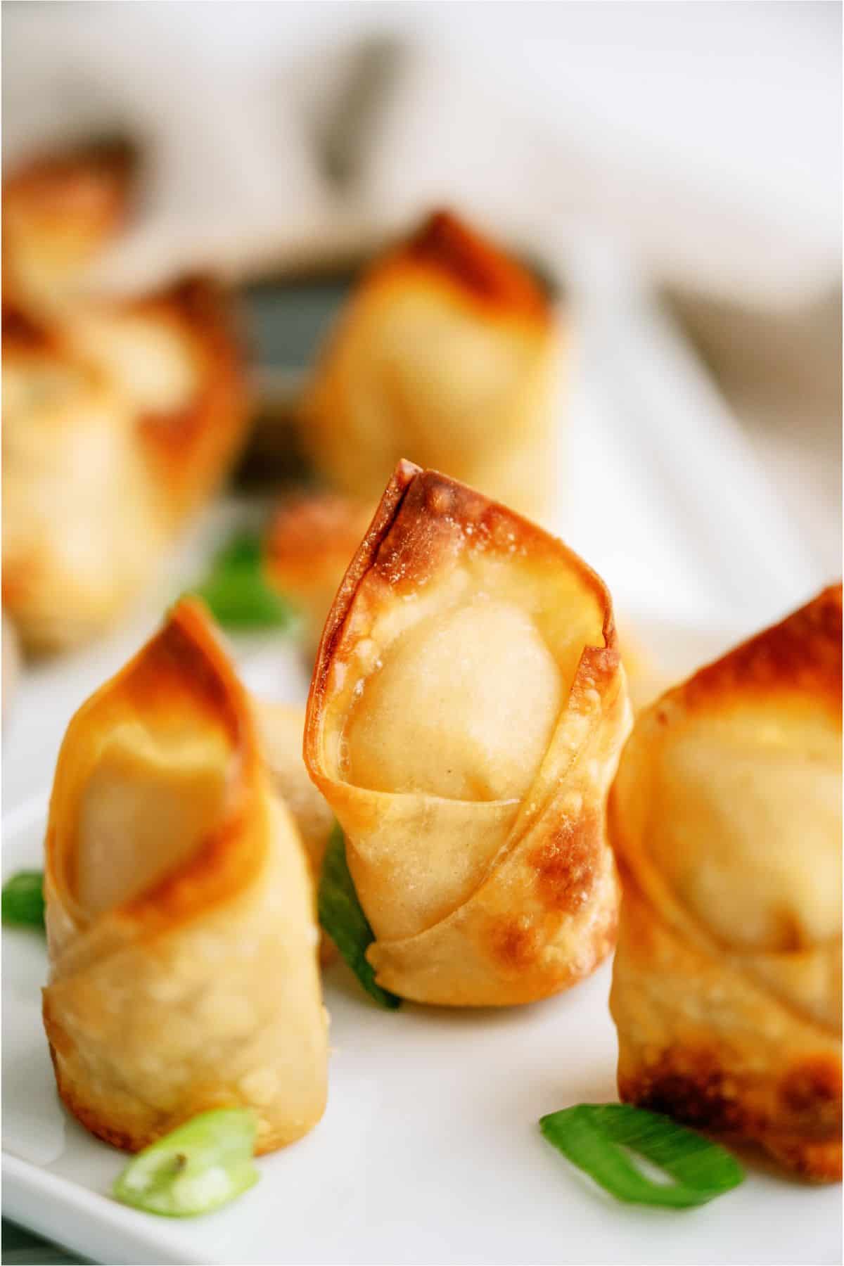 Close-up of crispy wontons on a white plate, garnished with chopped green onions.