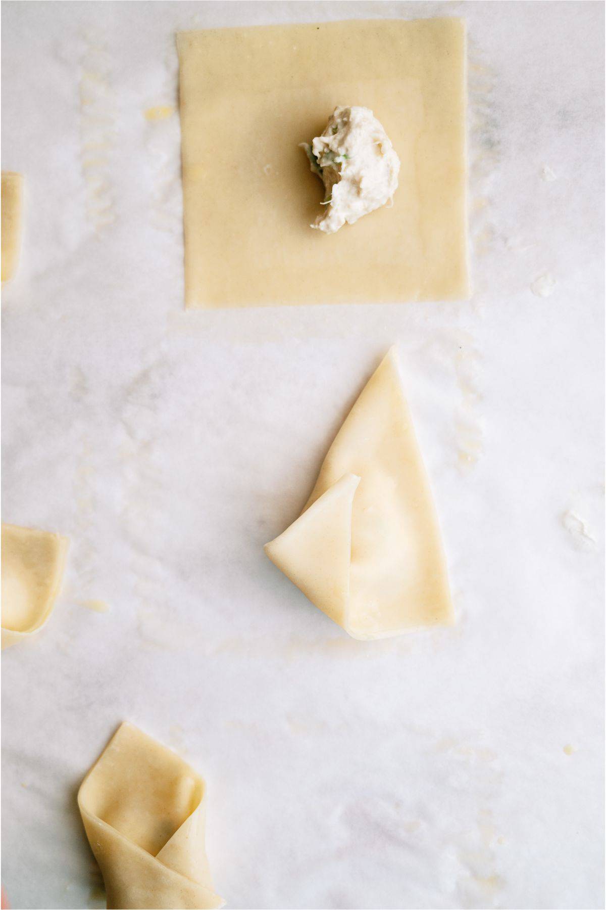 A sheet of dough with ricotta filling is shown, alongside a partially folded piece of dough on a lightly floured surface.