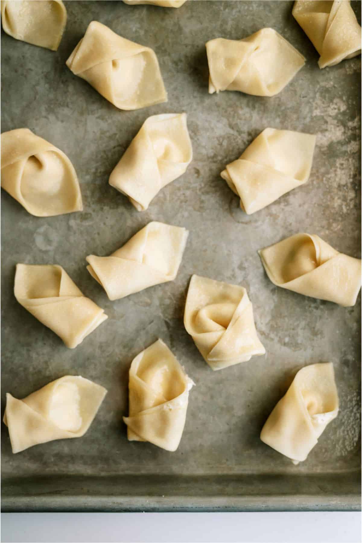 Raw wontons are neatly arranged in rows on a metal baking tray.