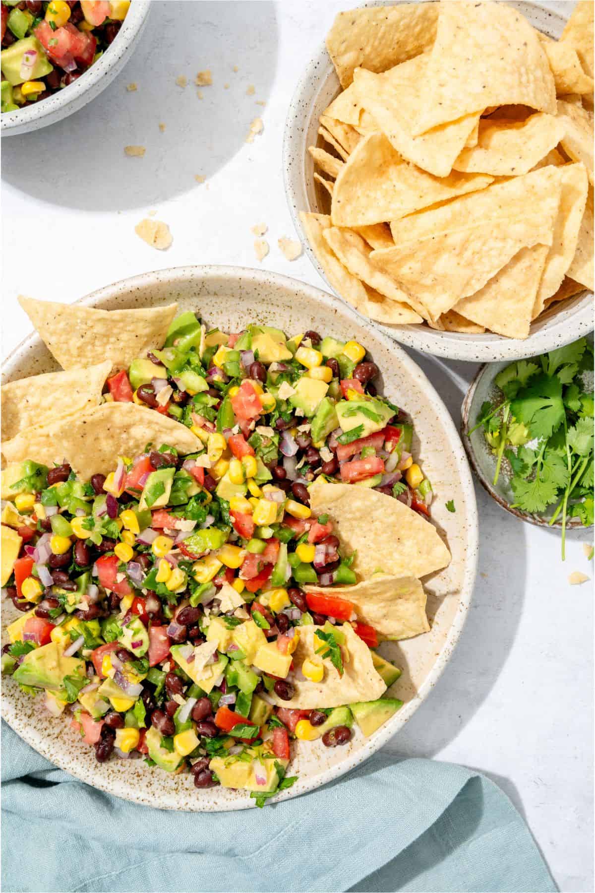 A bowl of Cowboy Caviar mixed with tortilla chips and a bowl of tortilla chips