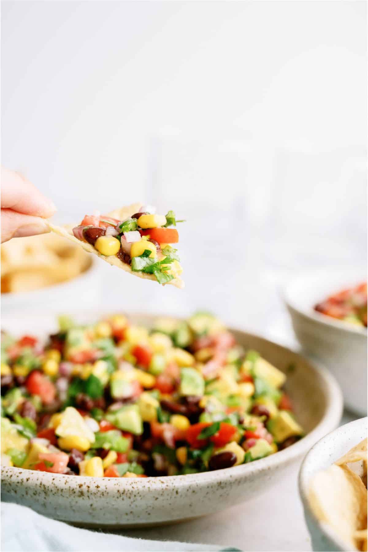A bowl of Cowboy Caviar with a hand holding a chip filled with the dip