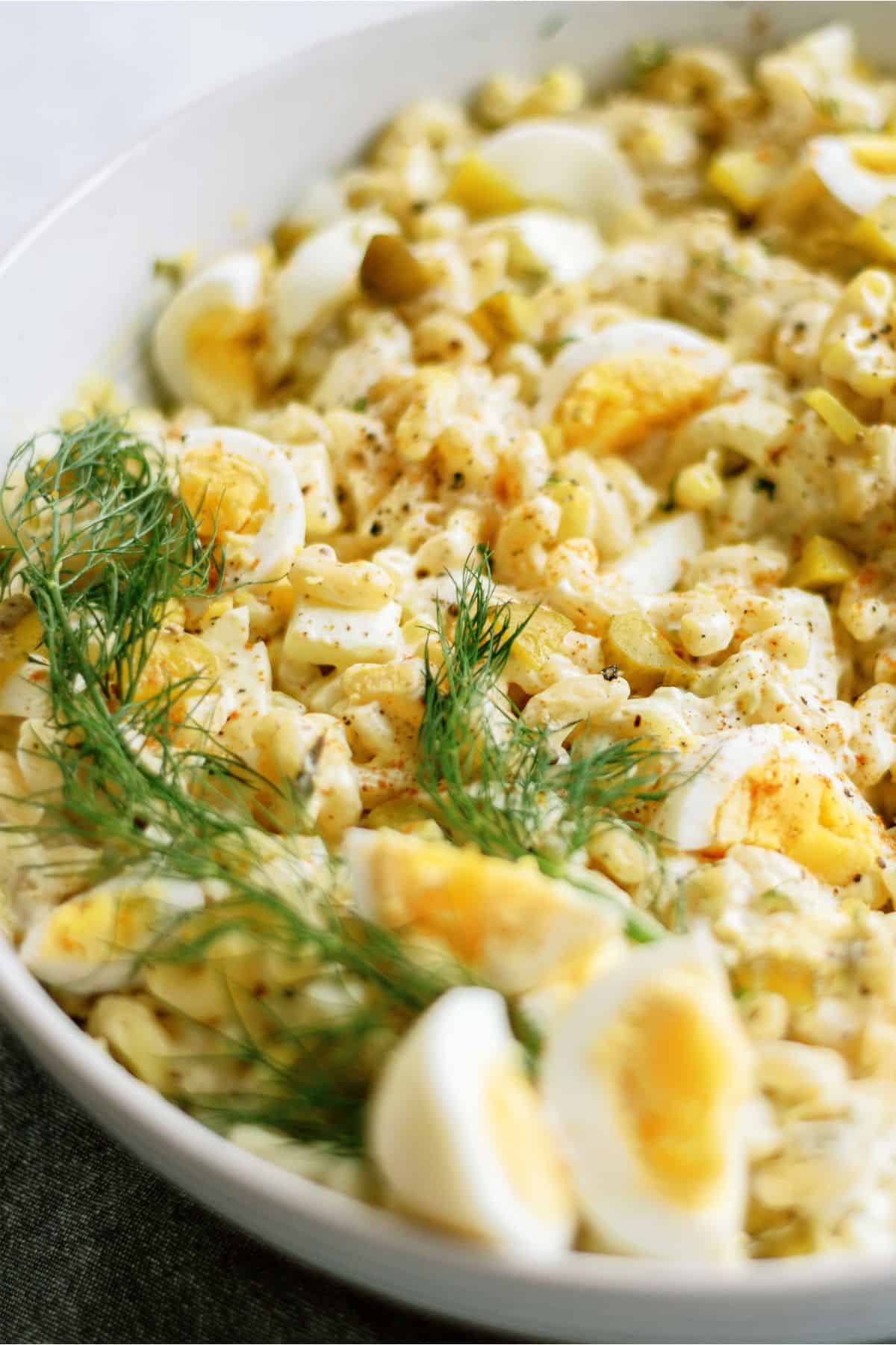 A bowl of pasta salad with chopped boiled eggs, herbs, and seasoning on top.