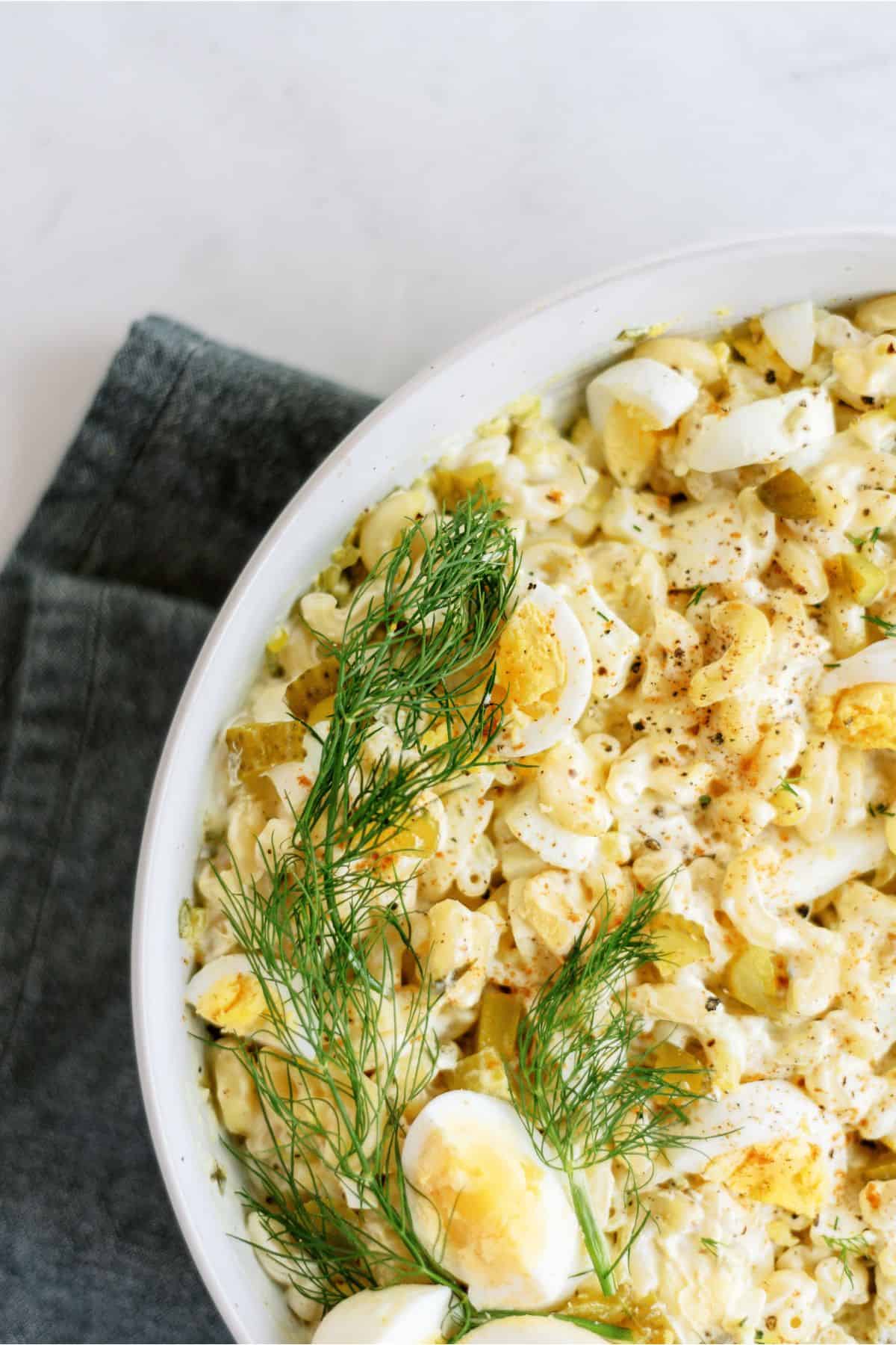Close-up of a bowl containing egg salad garnished with fresh dill. The salad sits on a dark gray cloth, showcasing chunks of boiled egg mixed with creamy dressing.