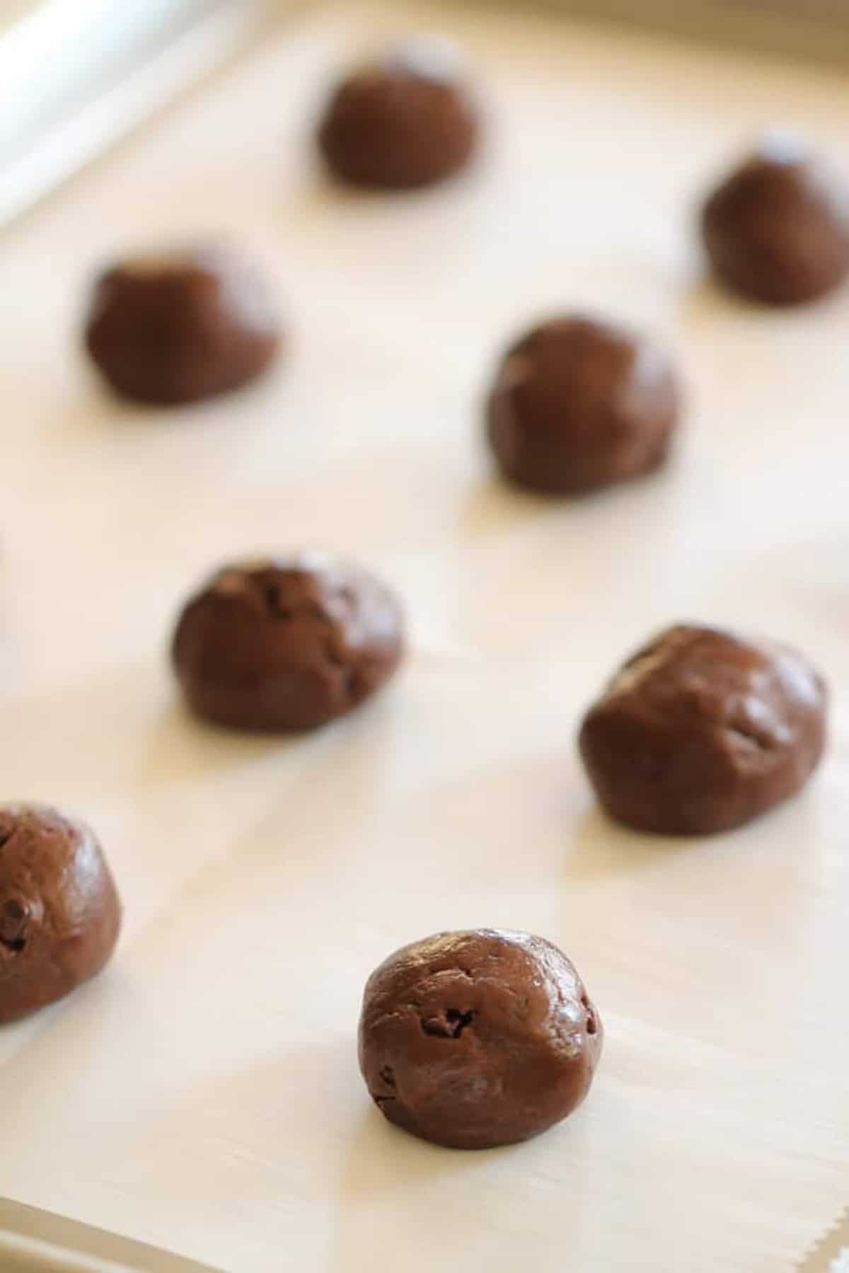 Close-up of nine chocolate cookie dough balls evenly spaced on a parchment-lined baking sheet.