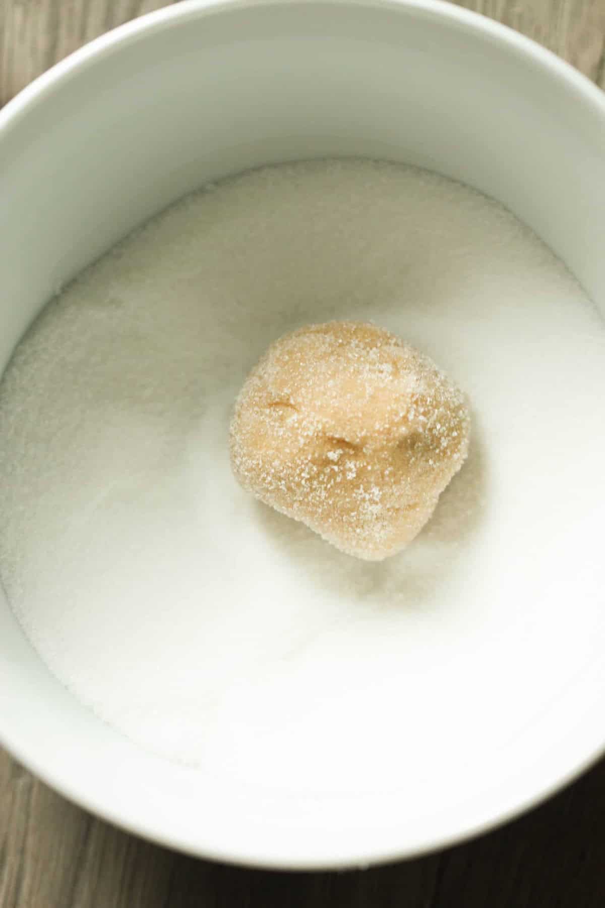 A dough ball sits in a bowl filled with white granulated sugar.