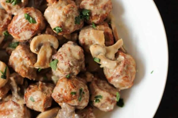 A white plate filled with meatballs and mushrooms in a creamy sauce, garnished with chopped parsley.