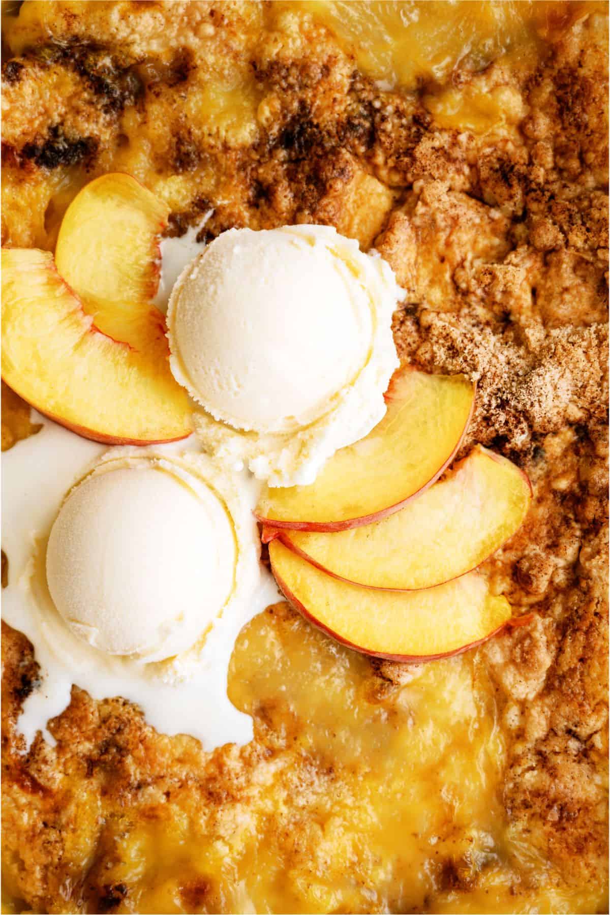 Peach cobbler topped with two scoops of vanilla ice cream and fresh peach slices.
