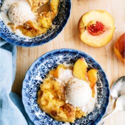 2 bowls of Peach Cobbler Dump Cake topped with ice cream. Fresh peaches cut in half.