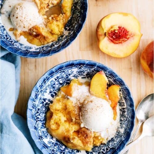 2 bowls of Peach Cobbler Dump Cake topped with ice cream. Fresh peaches cut in half.