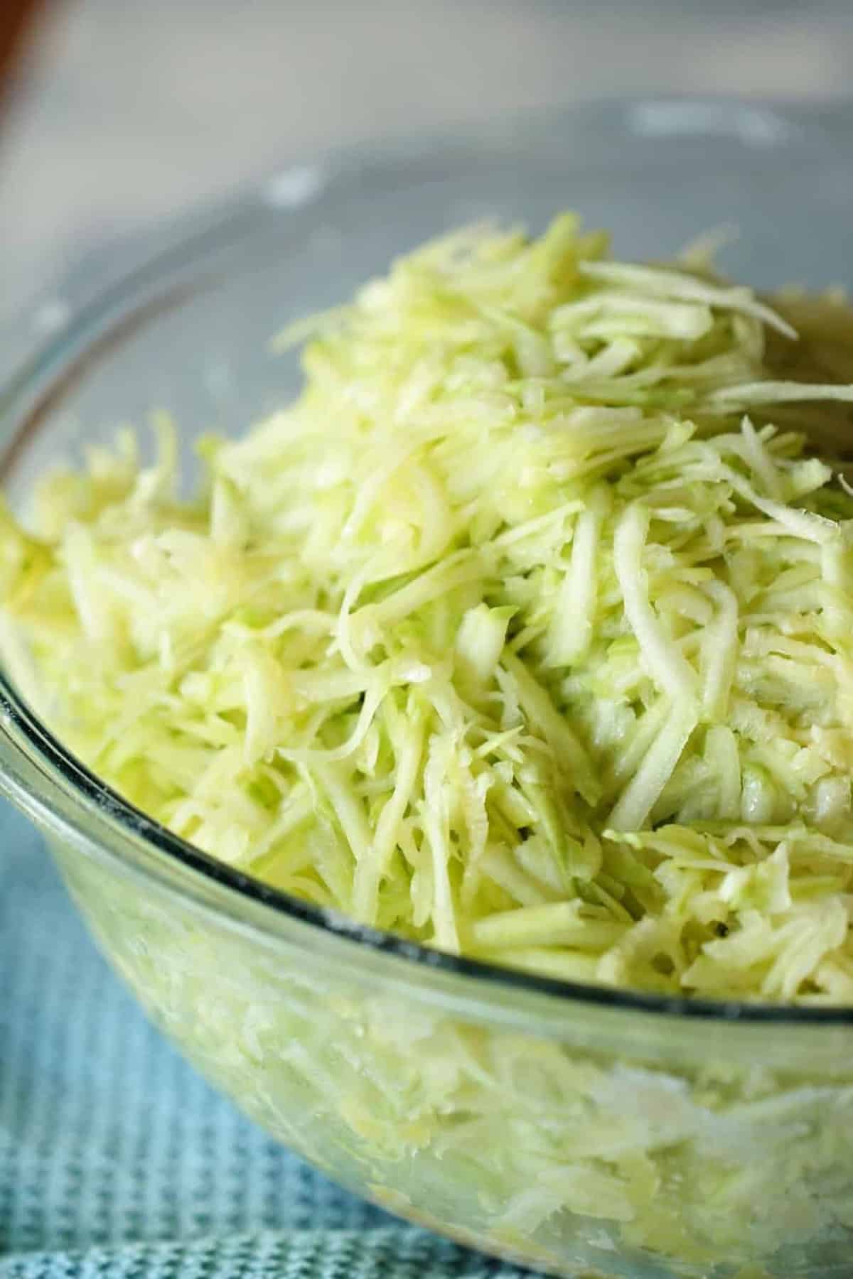 Close-up of a glass bowl filled with shredded green cabbage on a blue textured surface.