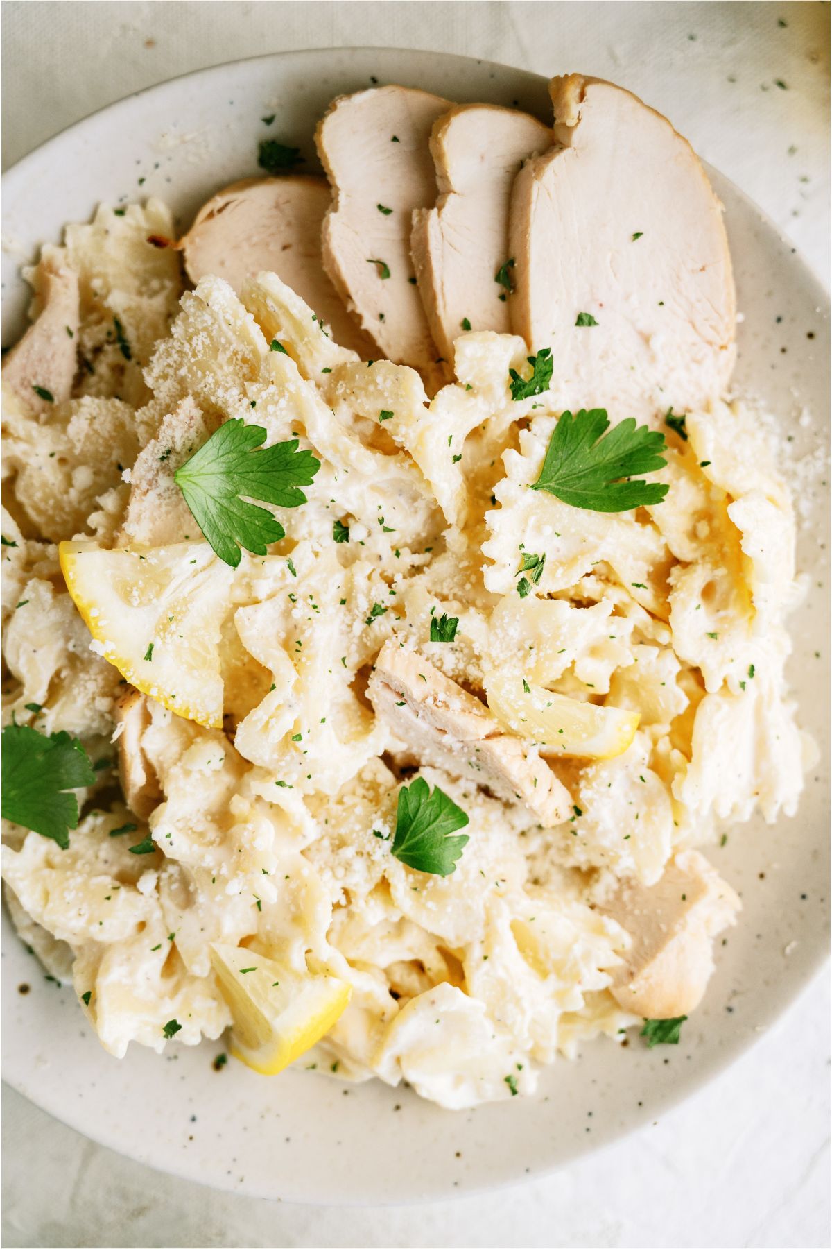 Top view of a plate of pasta with sliced chicken, topped with cheese.