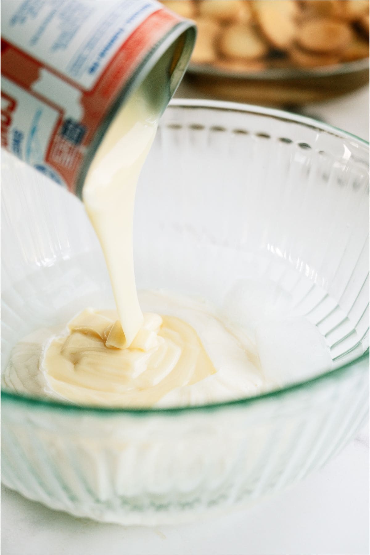 Pouring condensed milk into a glass bowl filled with cold water.