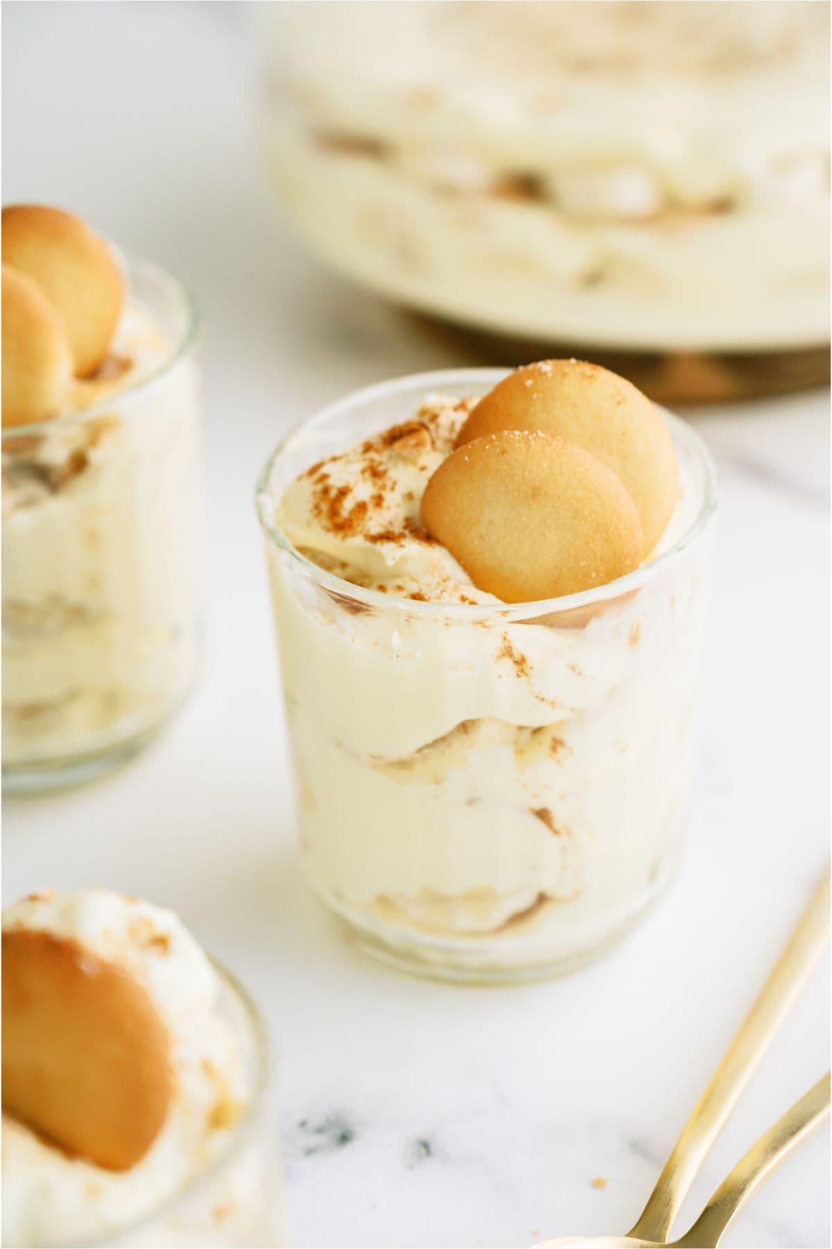 3 glass cups with servings of Copycat Magnolia Pudding in them, topped with nilla wafers. With the remaining Magnolia Pudding in a glass bowl in the background.