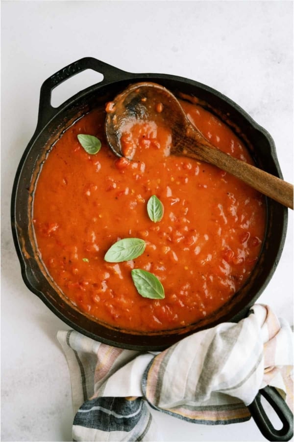 A large skillet on top of a striped towel filled with Tomato Gravy with a wooden spoon.