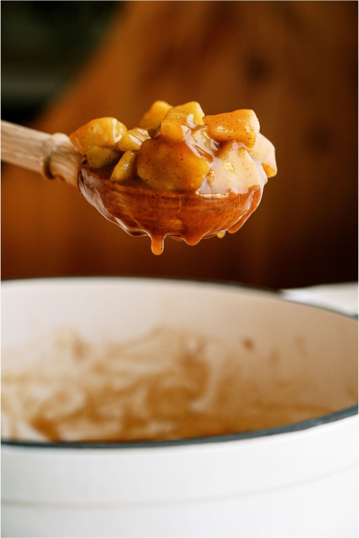 A wooden spoon lifting out a scoop of Apple Pie Filling out of a saucepan.