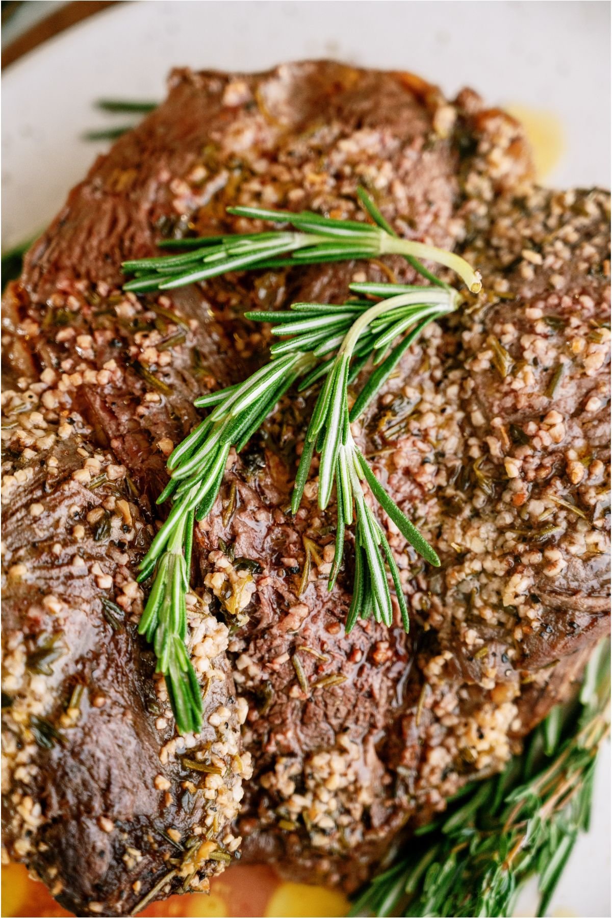 Top view of Garlic Butter Beef Roast with a sprig of fresh rosemary on top of the roast.