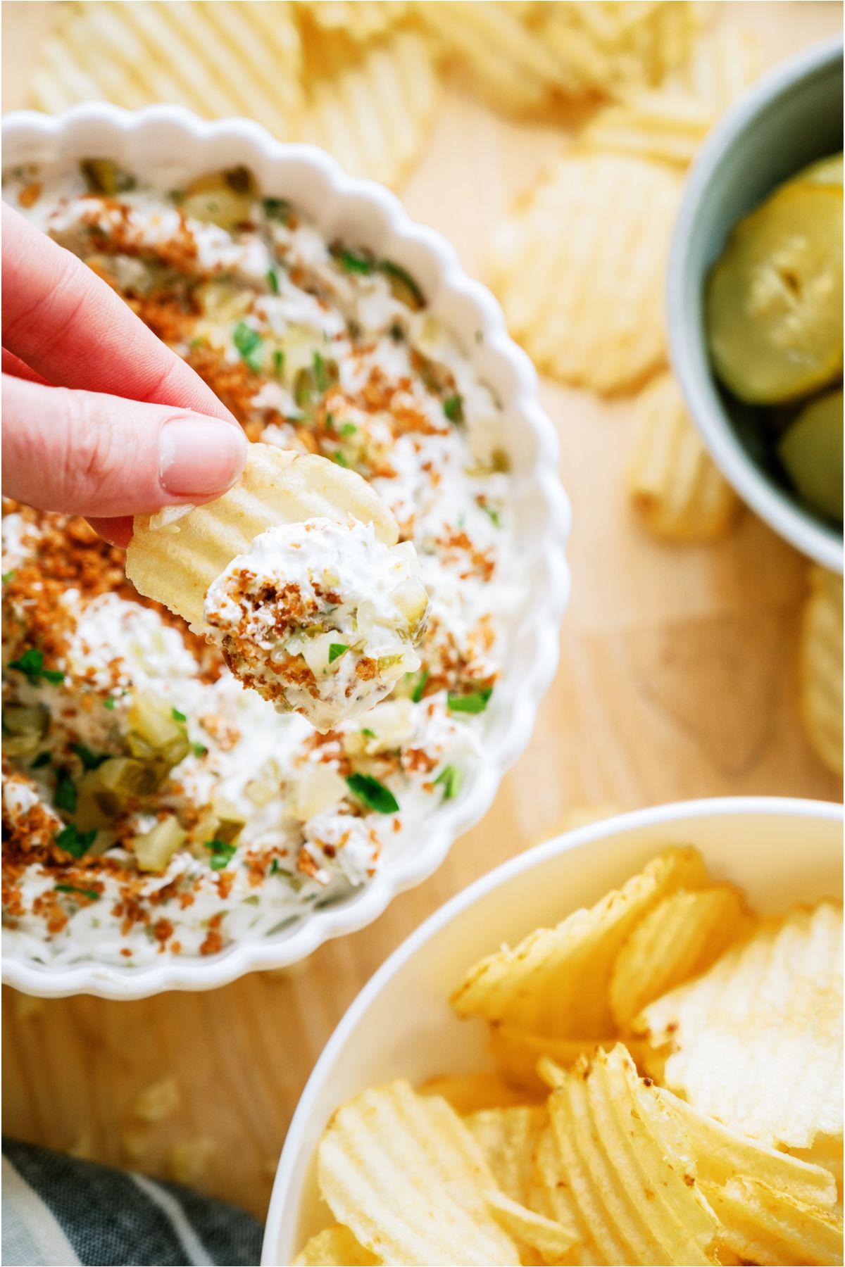 A hand dipping a chip in a bowl of Fried Pickle Dip.
