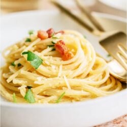 A white bowl of Classic Pasta Carbonara with af fork and spoon.