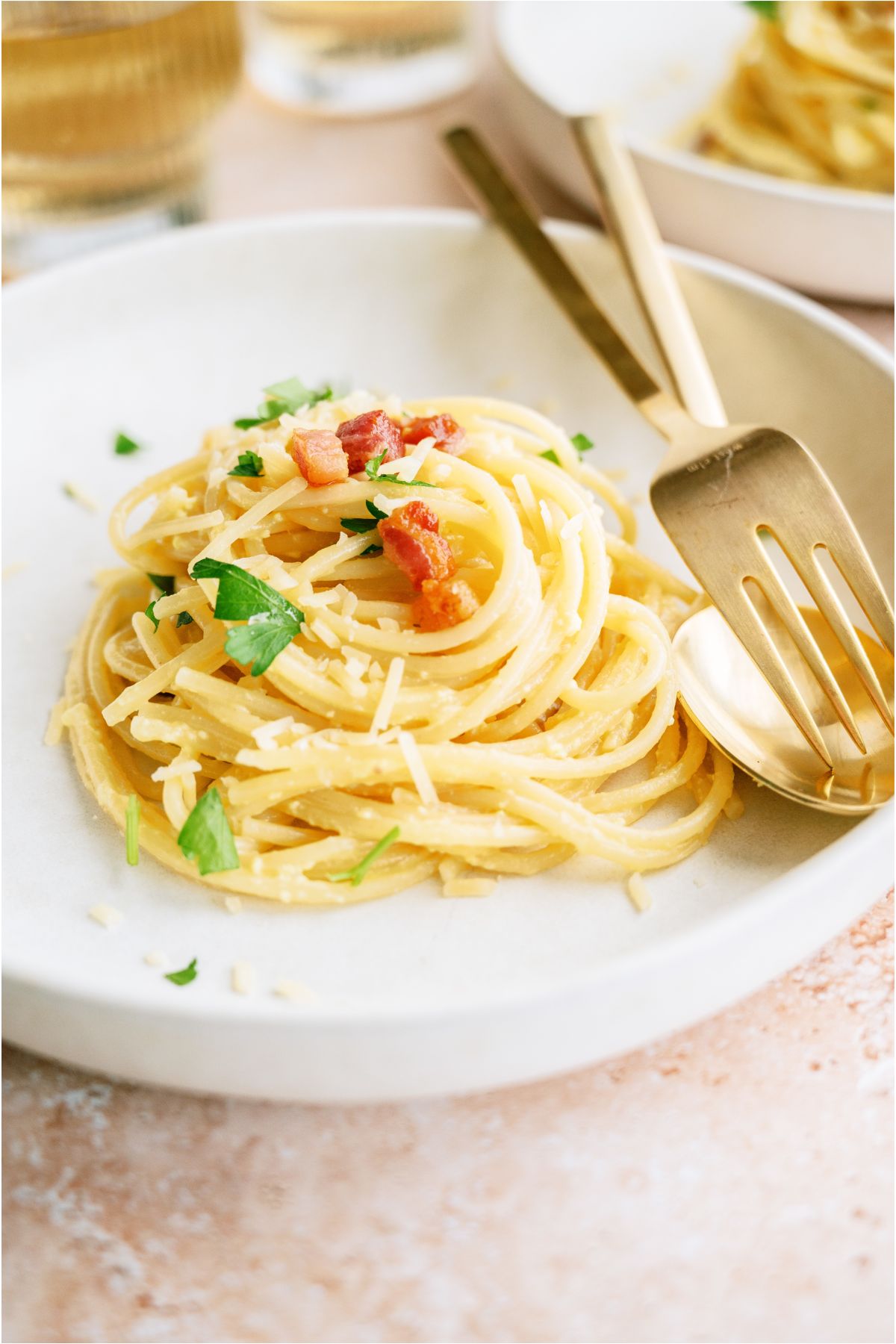 A small serving of Classic Pasta Carbonara on a white plate with a fork and spoon.