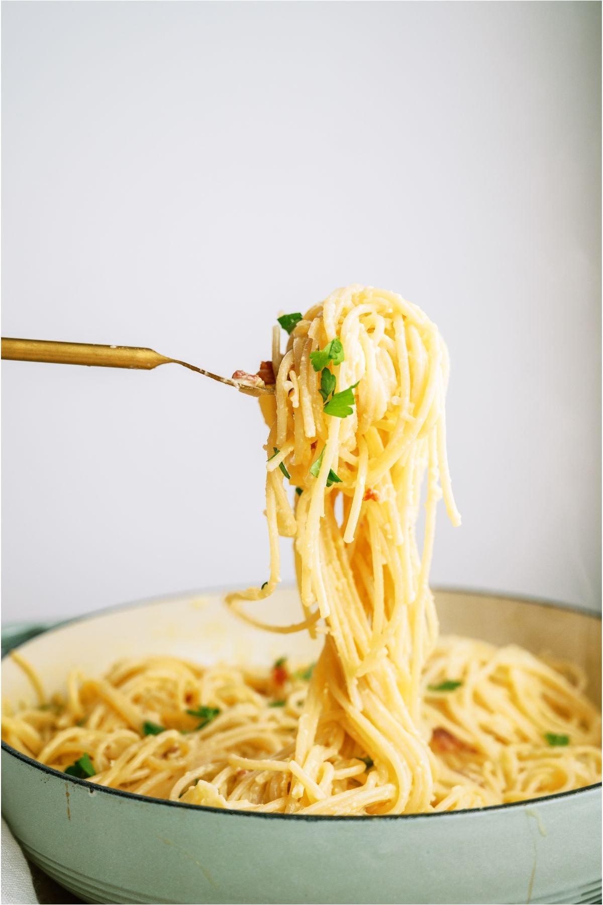 A fork holding up a large bite of Classic Pasta Carbonara from the plate below.