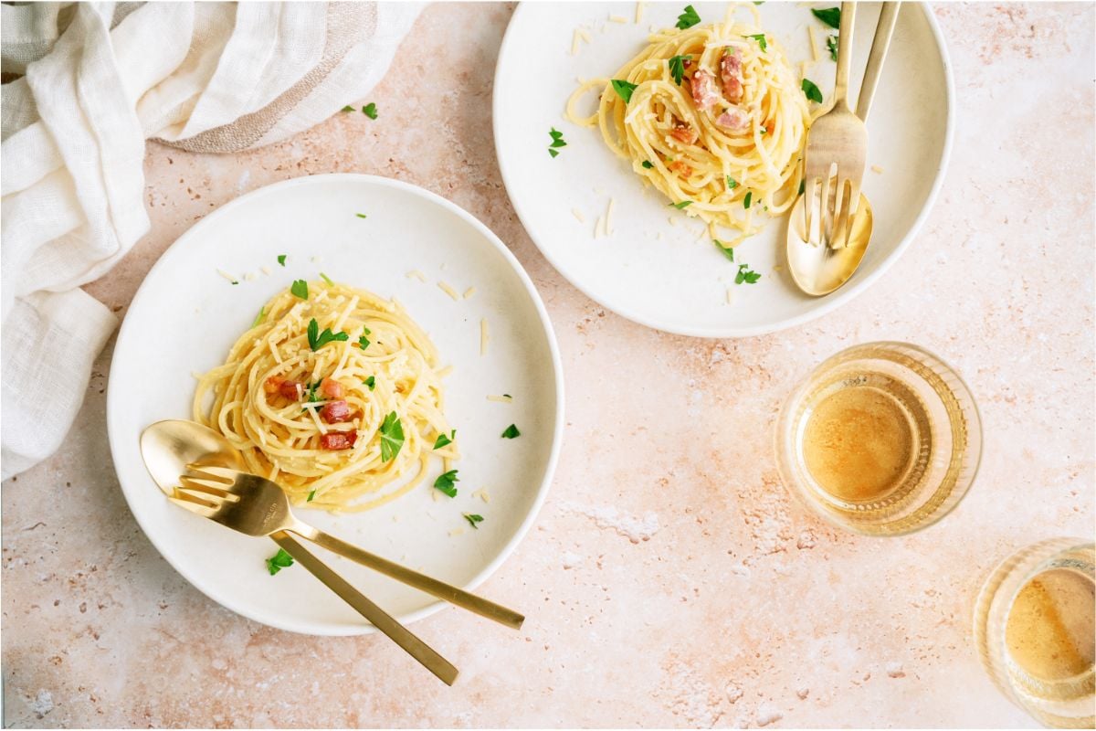 Top view of 2 plates of Classic Pasta Carbonara with forks and spoons.