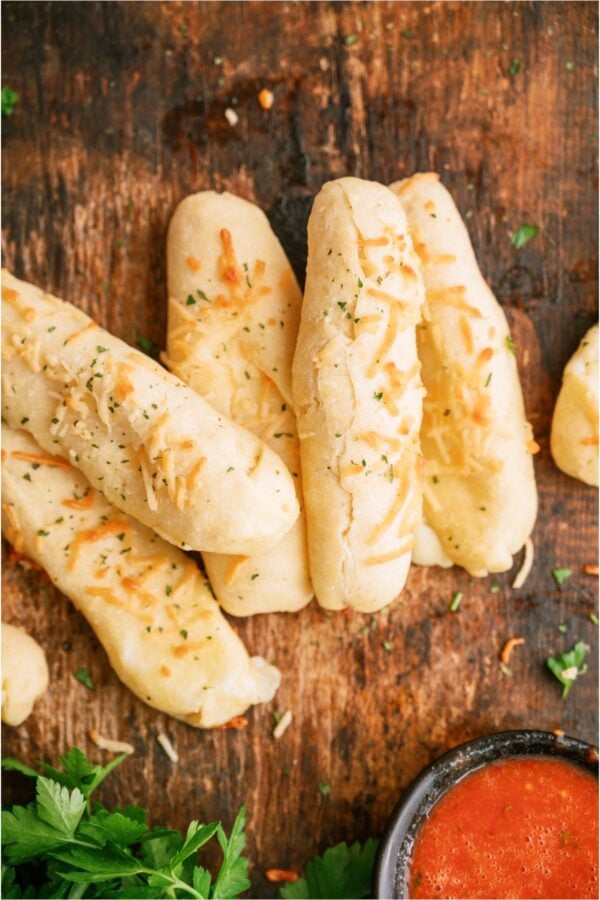 Copycat Bosco Sticks on a wooden background with a small bowl of marinara on the side.
