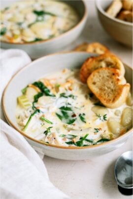 A bowl of Creamy Chicken Gnocchi Soup with two small slices of a baguette on top.