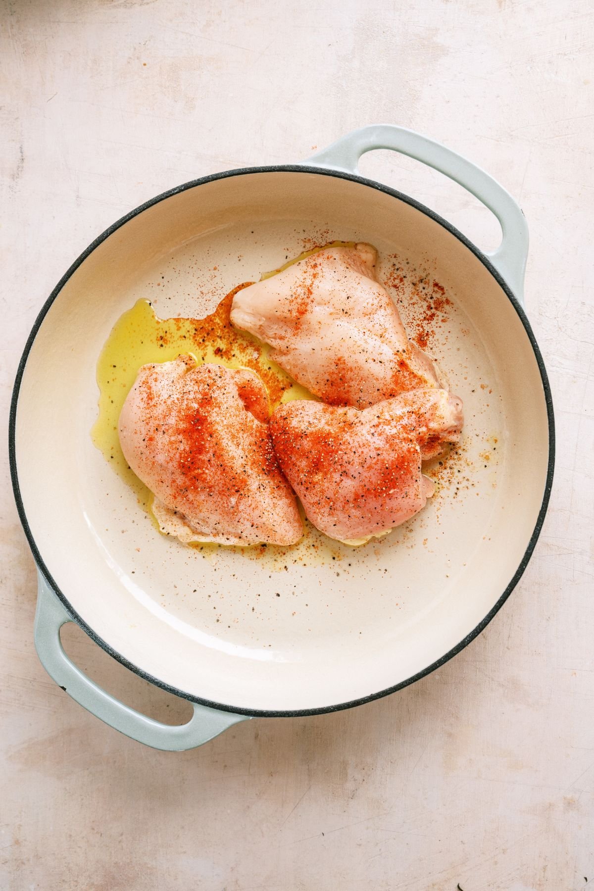 Small chicken breasts in a skillet with seasoning and olive oil.