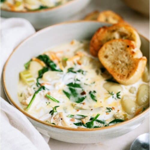 A bowl of Creamy Chicken Gnocchi Soup with two small slices of a baguette on top.