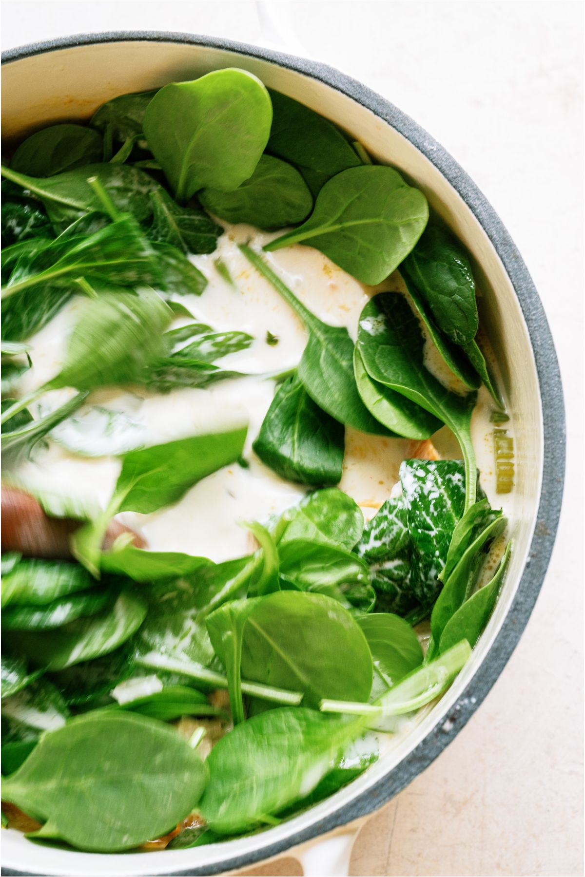 Fresh spinach leaves added to soup in the stockpot.