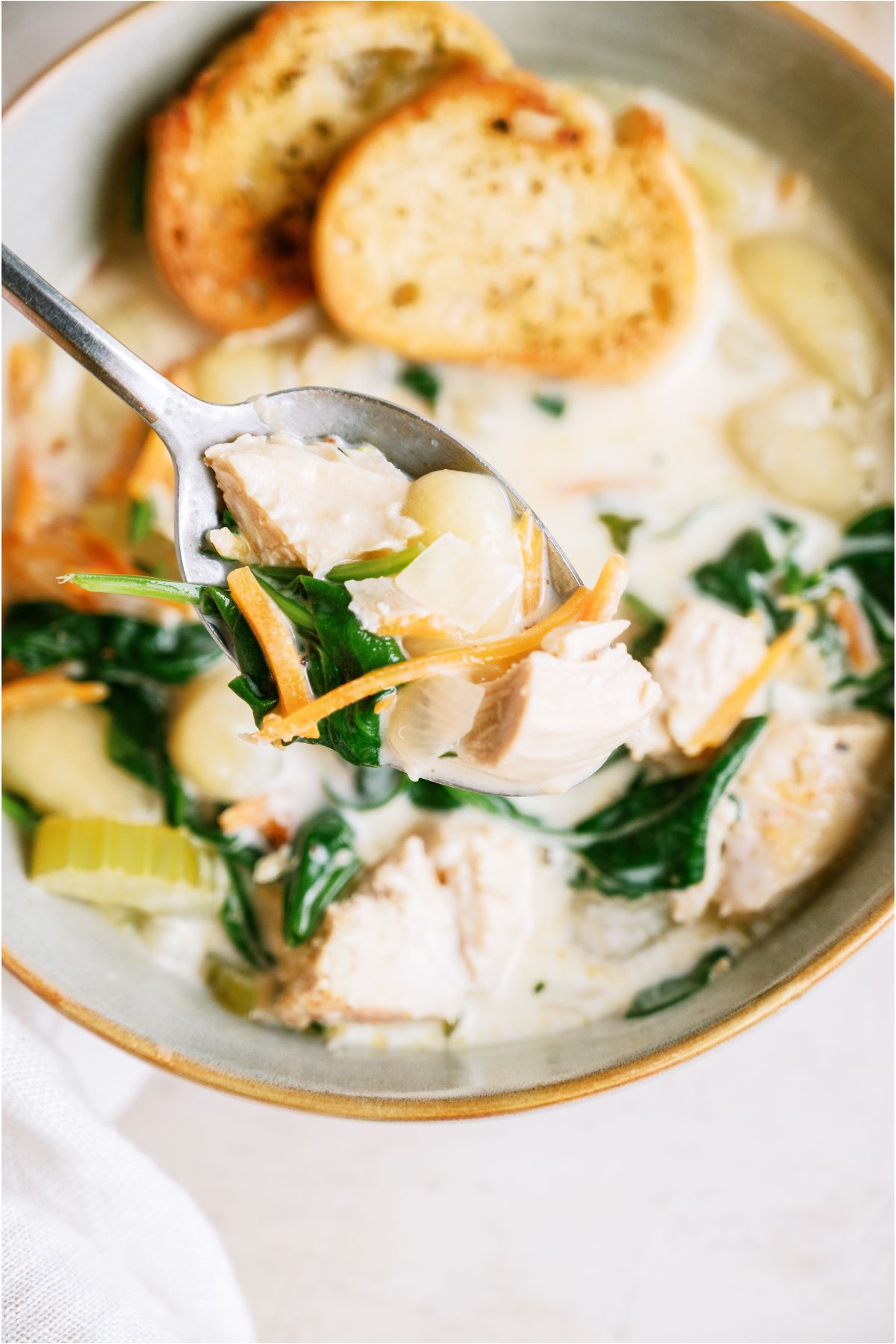 A bowl of Creamy Chicken Gnocchi Soup with a spoon holding up a bite.