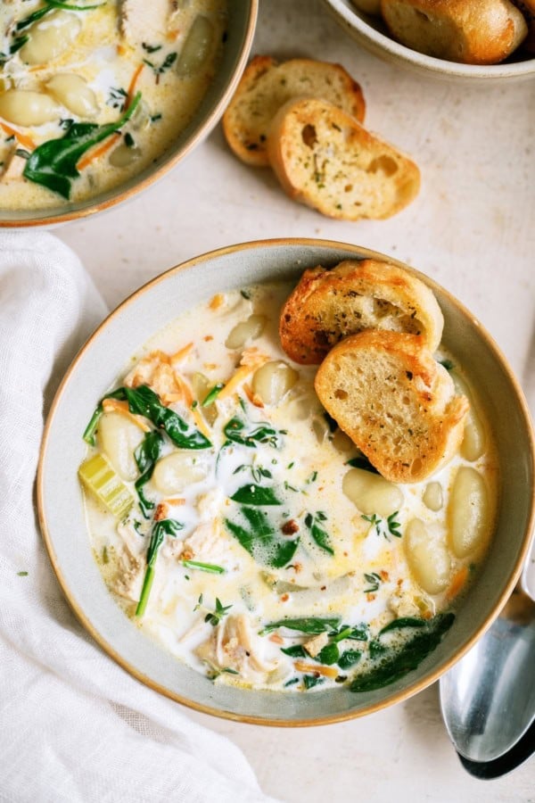 A bowl of Creamy Chicken Gnocchi Soup with two small slices of a baguette on top.