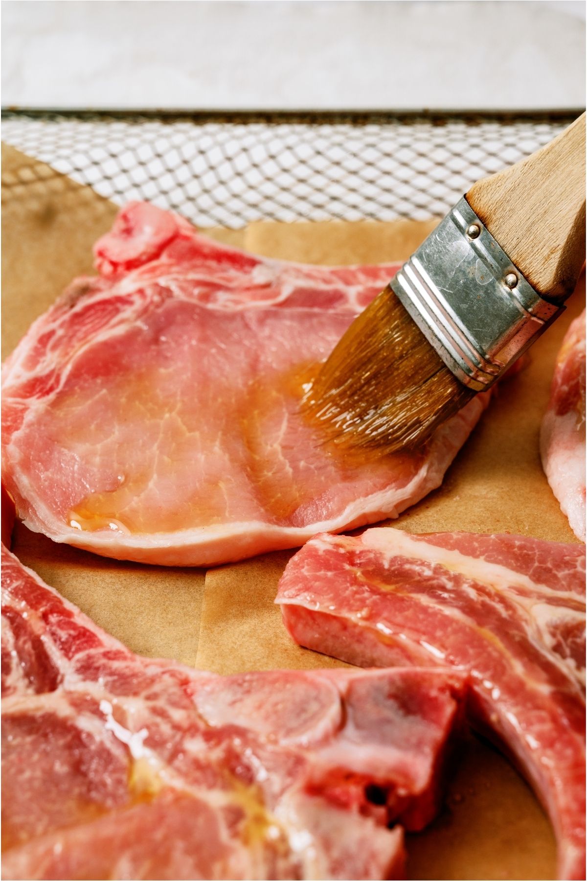 Brushing olive oil on raw pork chops.