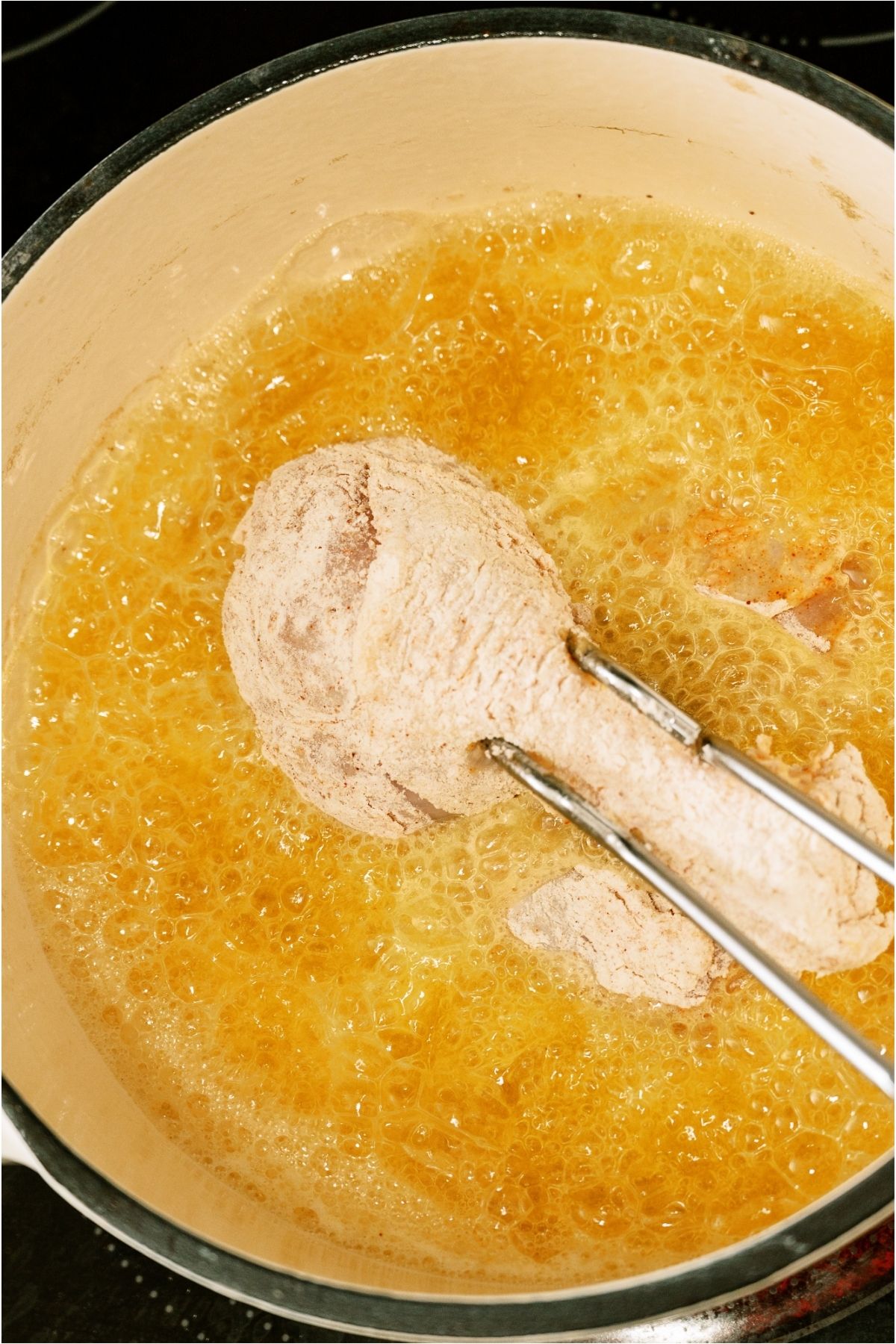 A pair of tongs placing the chicken pieces in a pan of hot oil.