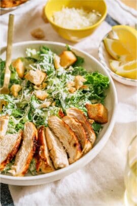 A bowl with Caesar salad topped with grilled chicken. A small bowl of shredded cheese in the background.