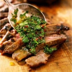 Chimichurri Sauce being spooned over sliced steak on a cutting board.