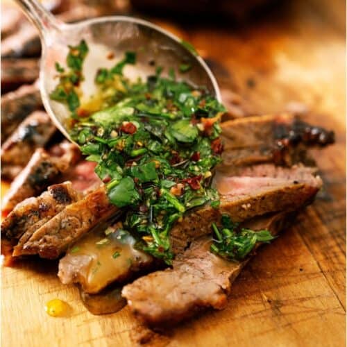 Chimichurri Sauce being spooned over sliced steak on a cutting board.