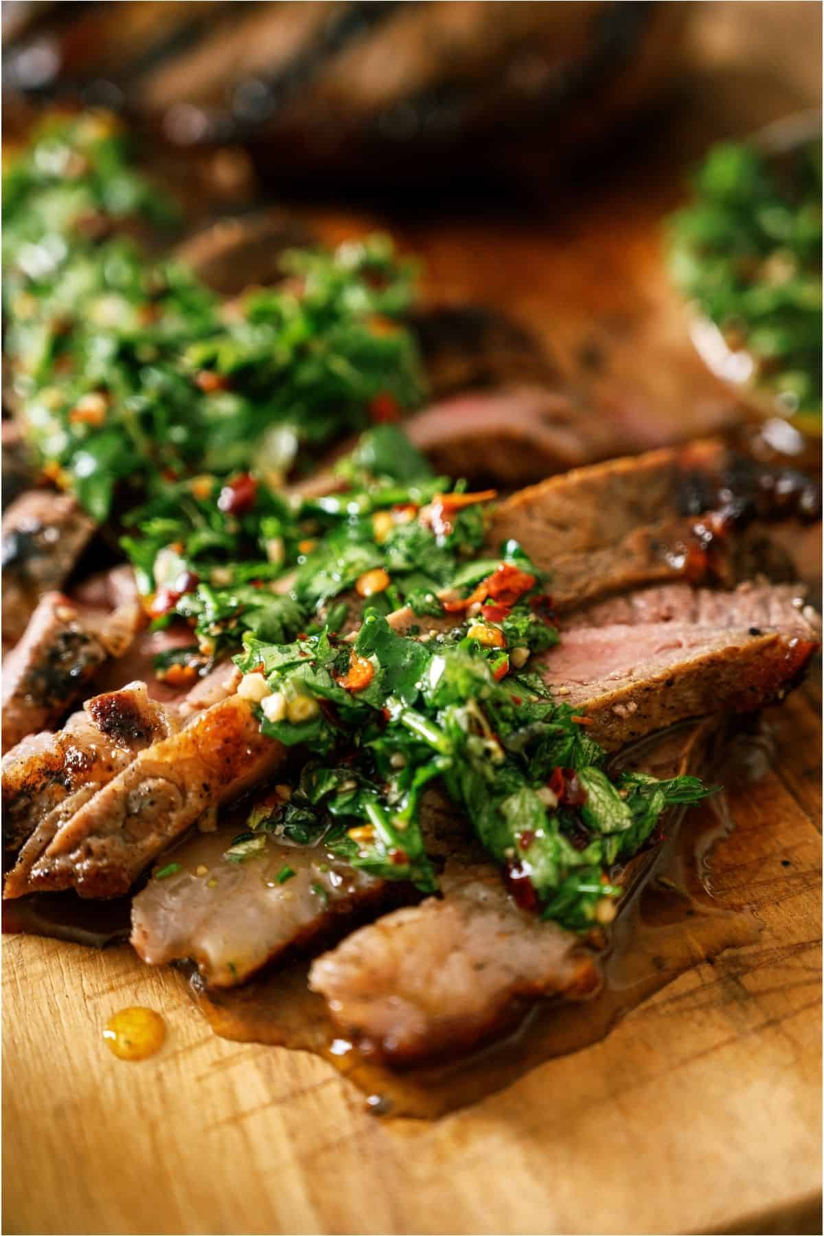 Sliced steak on a cutting board with Chimichurri Sauce on top.