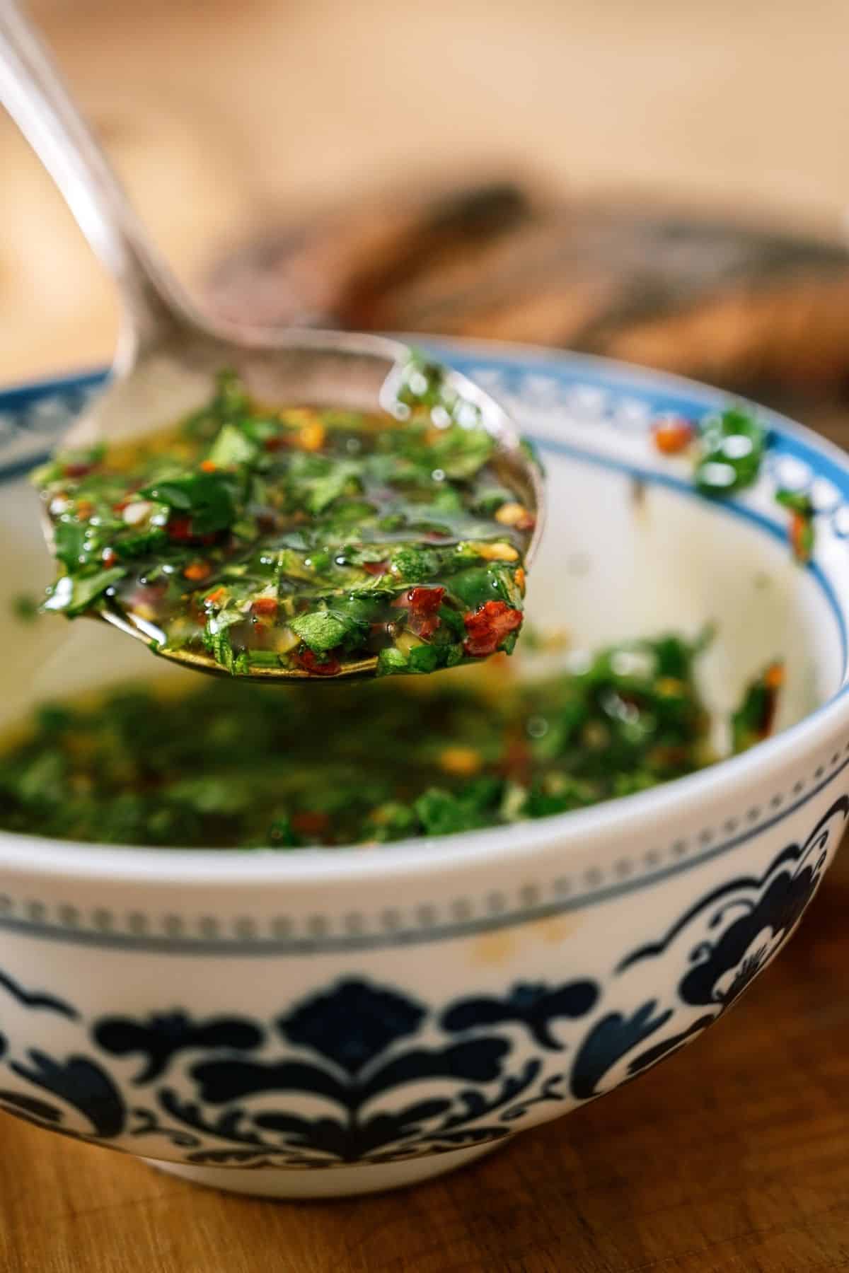 A bowl of Chimichurri Sauce with a spoon lifting a scoop out.