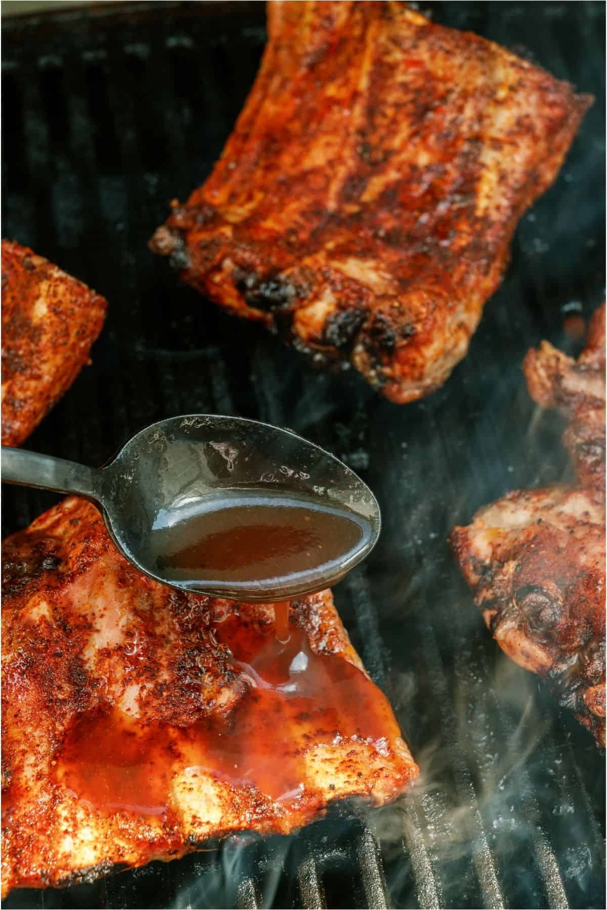 Spooning BBQ sauce over Grilled Baby Back Ribs on the grill.