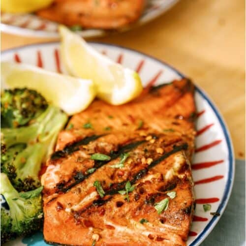 Grilled salmon and broccoli on a plate with lemon wedges.