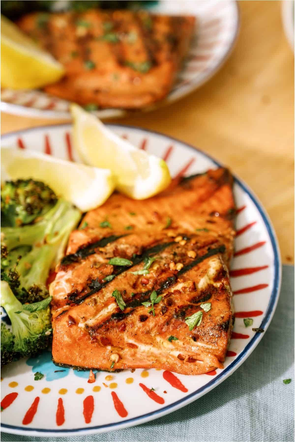 Grilled salmon and broccoli on a plate with lemon wedges.