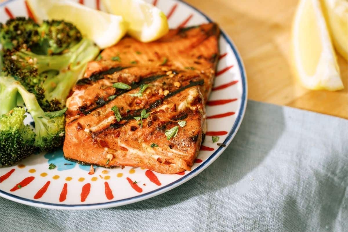 A plate with grilled salmon, broccoli and lemon wedges.