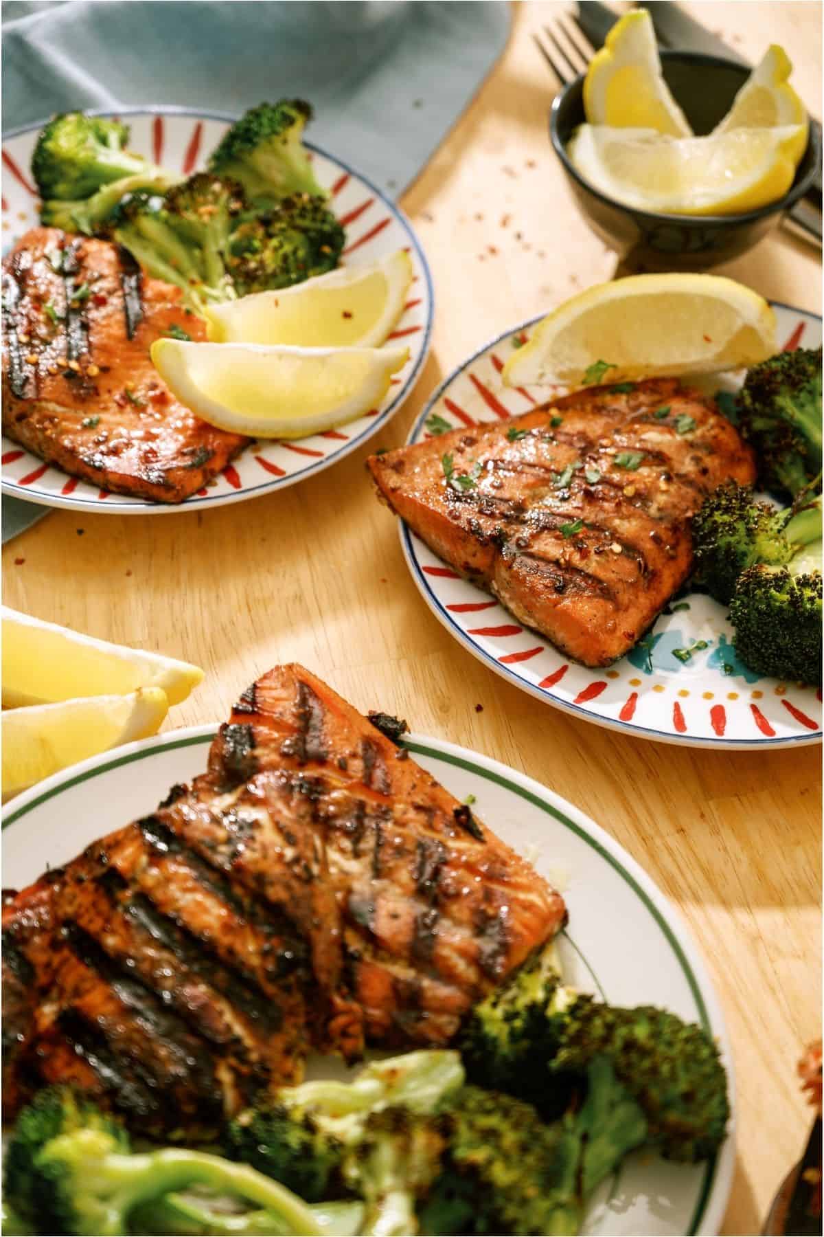 Top view of 3 plates of Grilled Salmon with broccoli and lemon wedges.